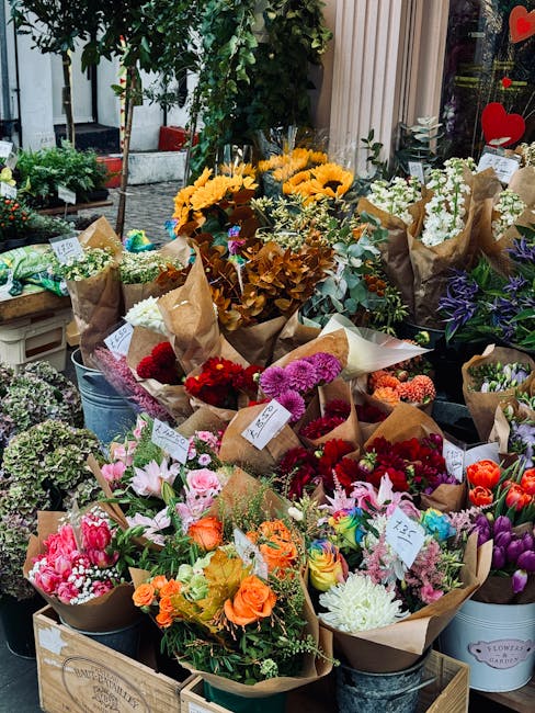A vibrant display of freshly arranged floral bouquets on a street-side flower stall, featuring a variety of seasonal flowers wrapped in brown kraft paper and positioned in metal buckets and wooden cra